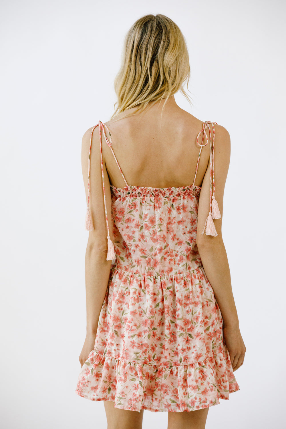 Back view of a woman wearing a vibrant pink floral print mini dress on a white background