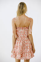 Back view of a woman wearing a vibrant pink floral print mini dress on a white background