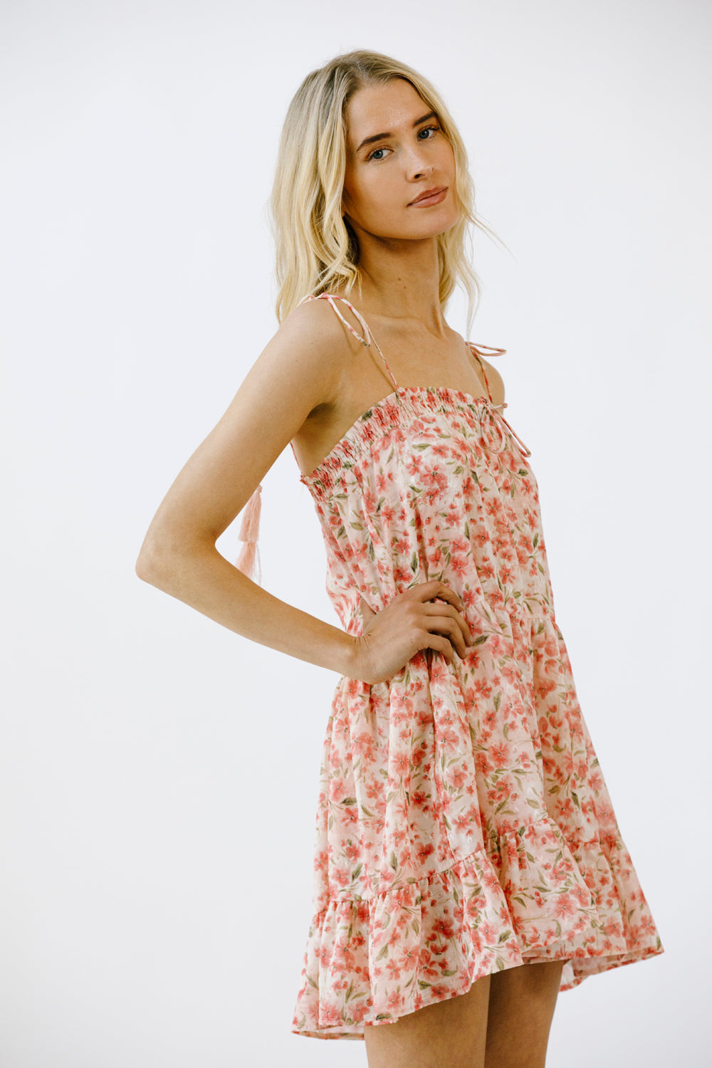 Side view of a woman wearing a vibrant pink floral print mini dress on a white background