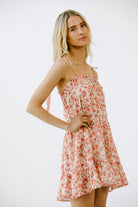 Side view of a woman wearing a vibrant pink floral print mini dress on a white background