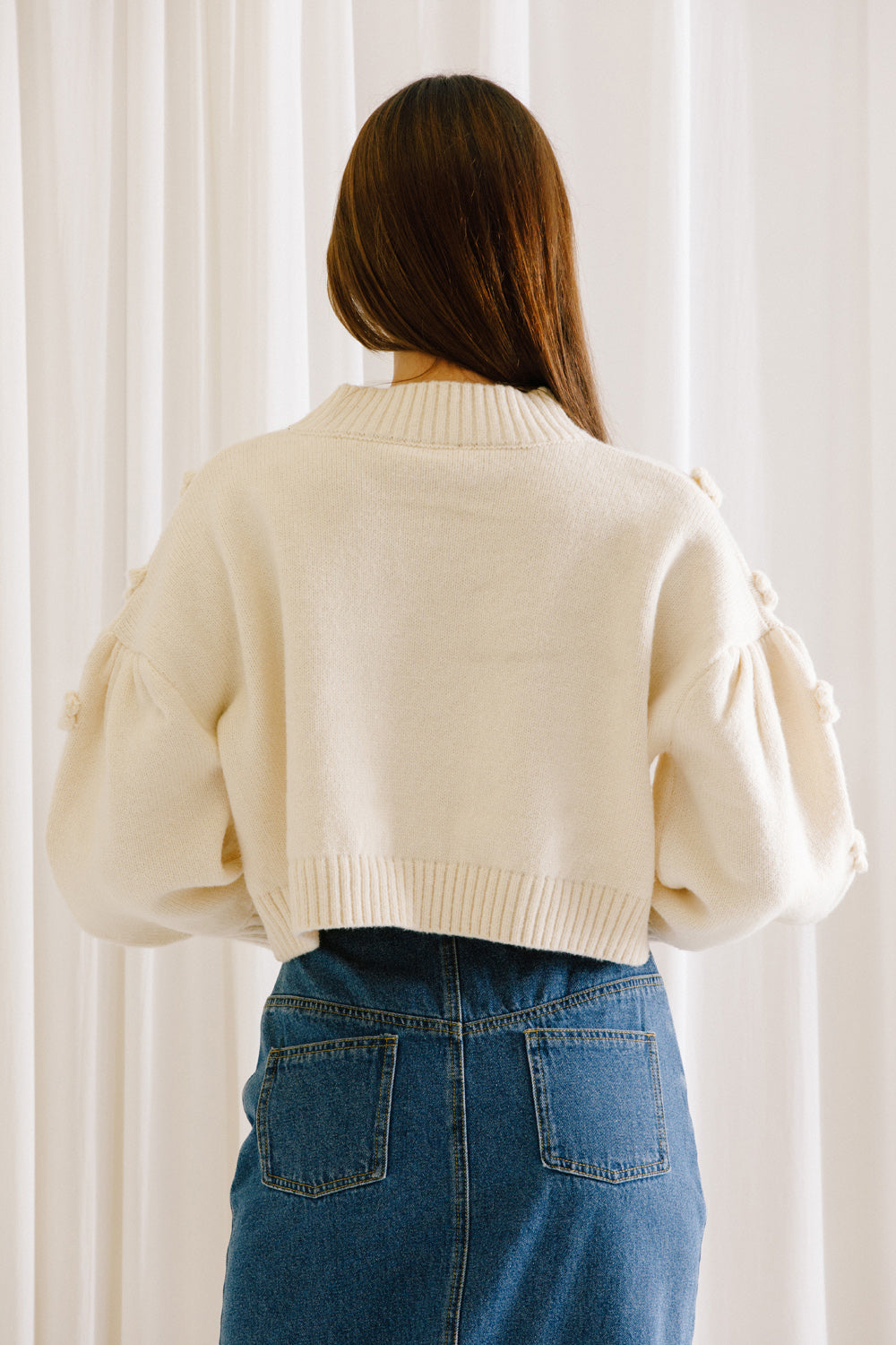 Woman showing the back of a cropped sweater in cream