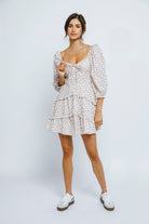 Woman wearing a ditsy floral print dress with puffy sleeves and white sneakers against a plain background