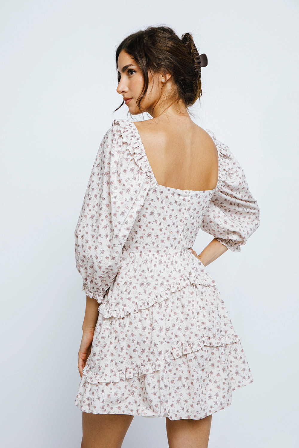 Back view of a woman wearing a ditsy floral print dress with puffy sleeves against a plain background