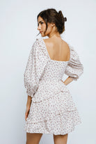 Back view of a woman wearing a ditsy floral print dress with puffy sleeves against a plain background