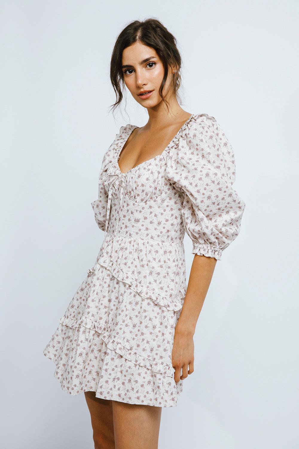 Woman wearing a ditsy floral print dress with puffy sleeves against a plain background
