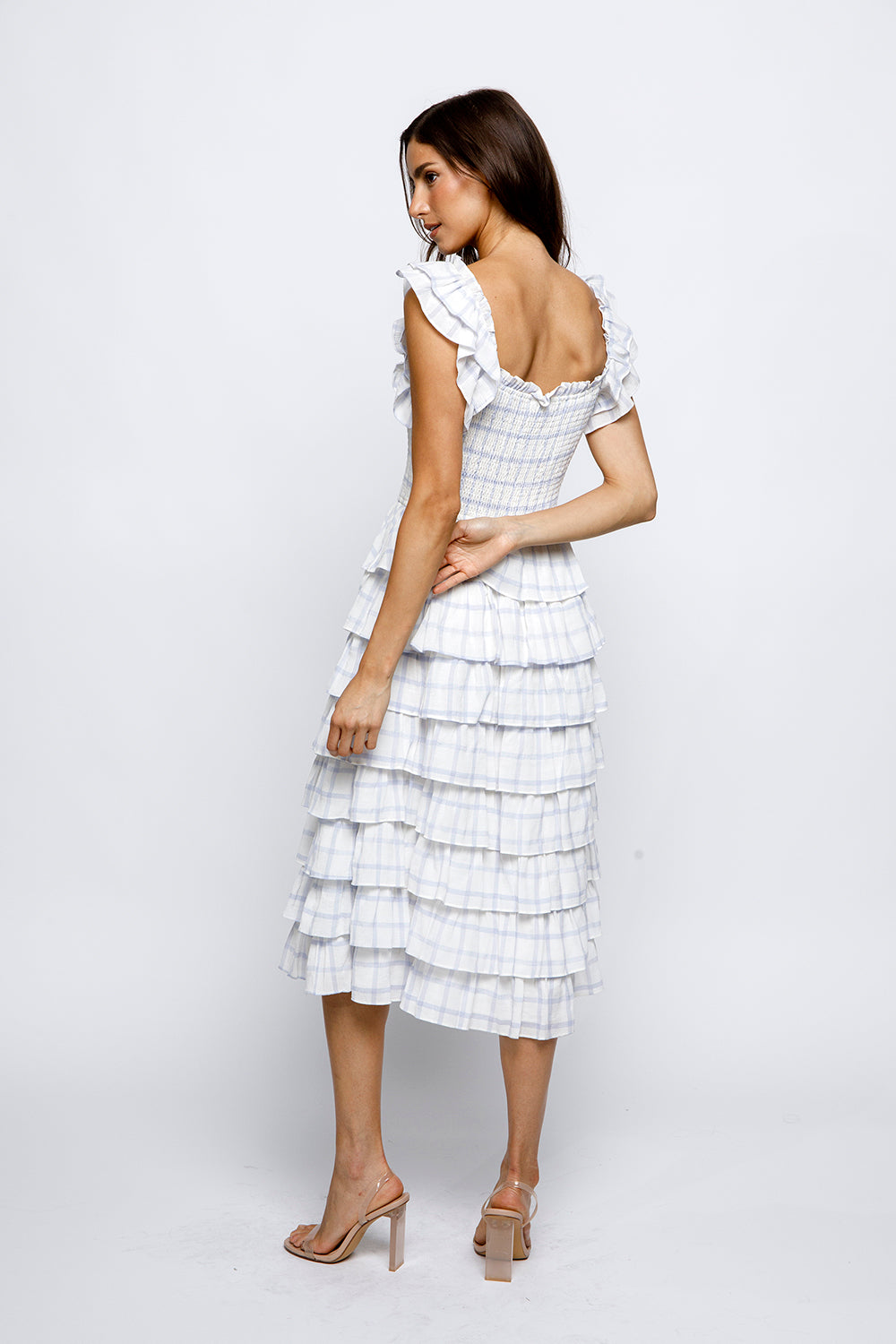 Woman wearing a white checkered dress with ruffled sleeves on a white background.