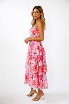 Side view of a woman wearing a vibrant pink floral dress on a white background