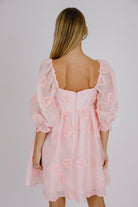 Back view of a woman wearing a pink dress with heart patterns on a plain background