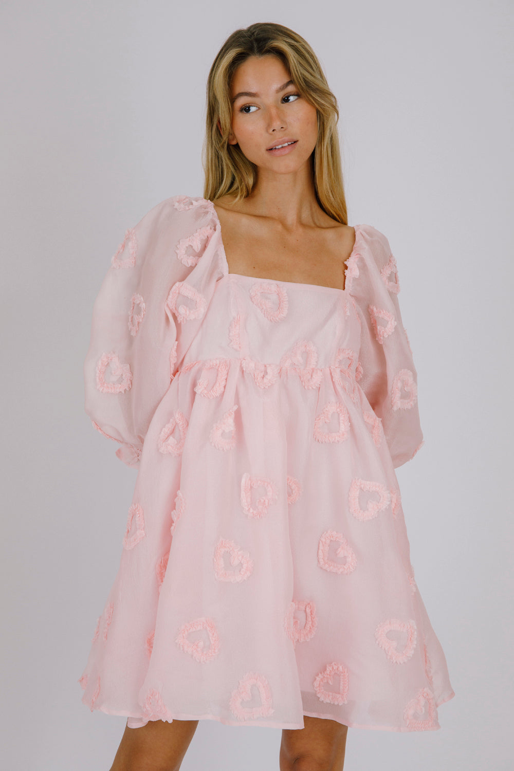 Woman wearing a pink dress with heart patterns on a plain background
