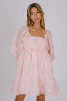 Woman wearing a pink dress with heart patterns on a plain background
