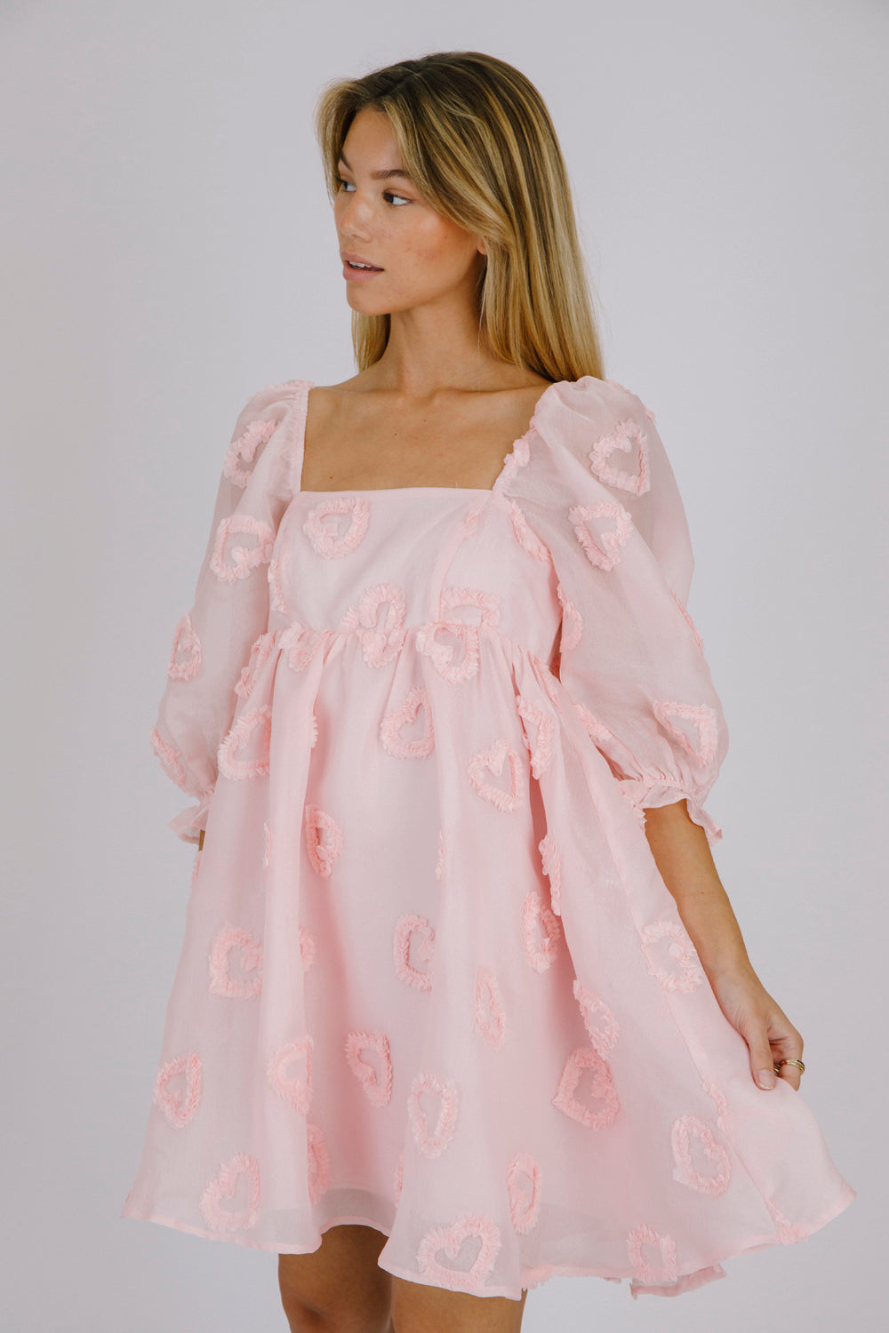Side view of a woman wearing a pink dress with heart patterns on a plain background