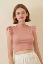 Woman wearing a pink top with ruffled sleeves against a beige background