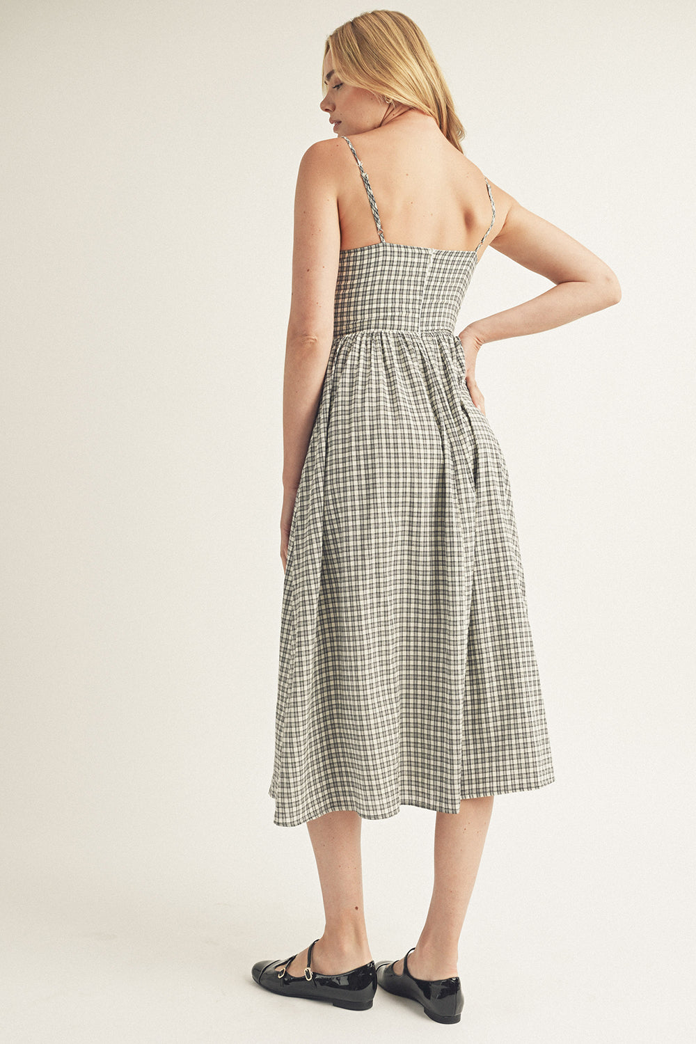 Back view of a woman wearing a black and white checkered dress on a plain background