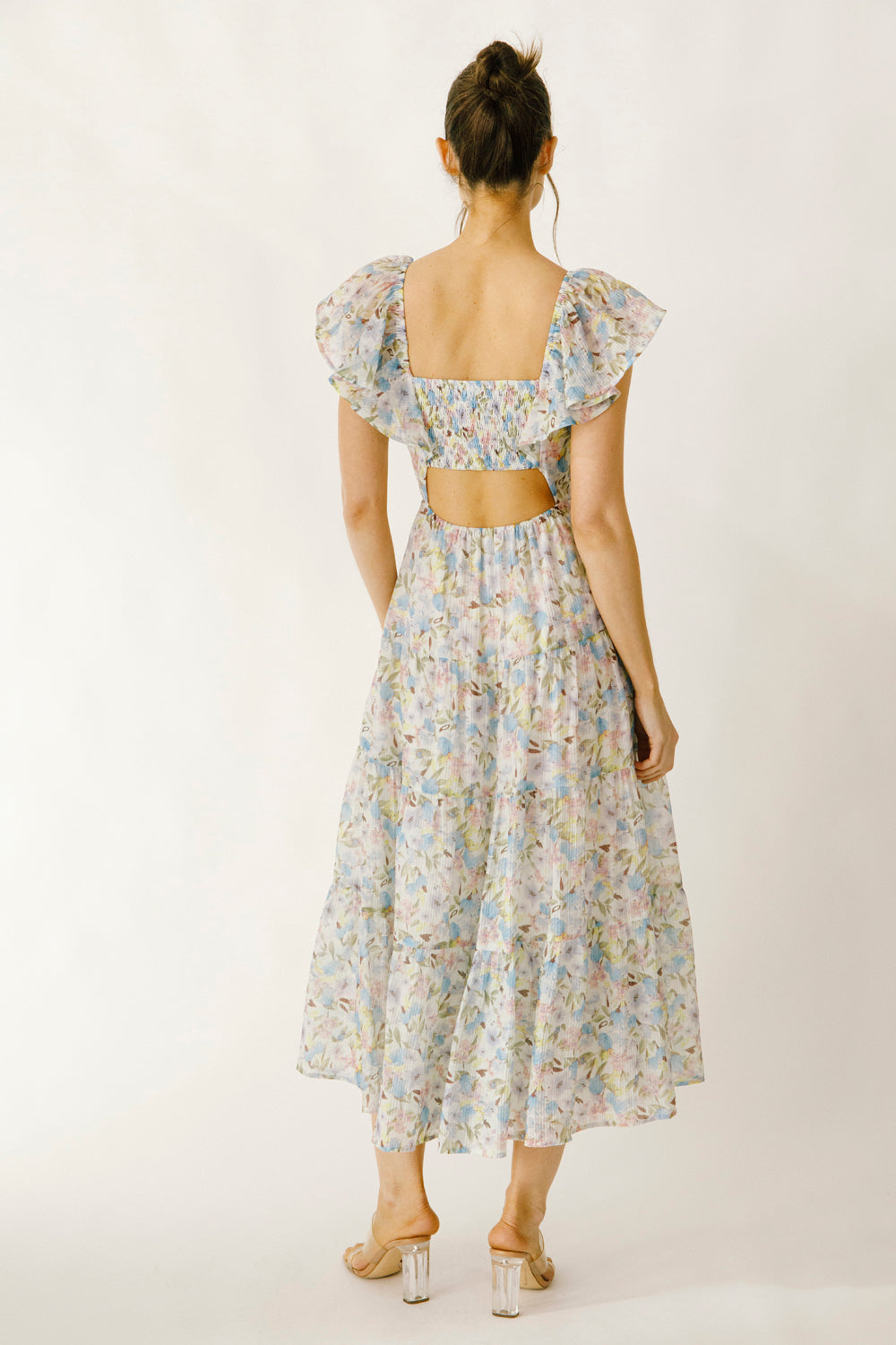 Back view of a woman wearing a blue and pink floral dress on a white background