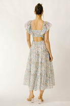 Back view of a woman wearing a blue and pink floral dress on a white background