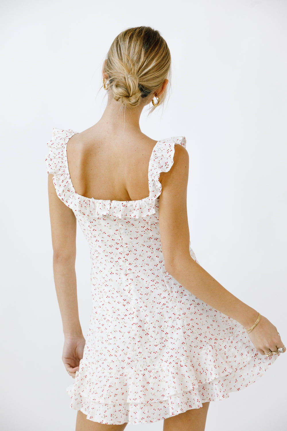 Back view of a woman wearing a white and red floral dress with a plain background