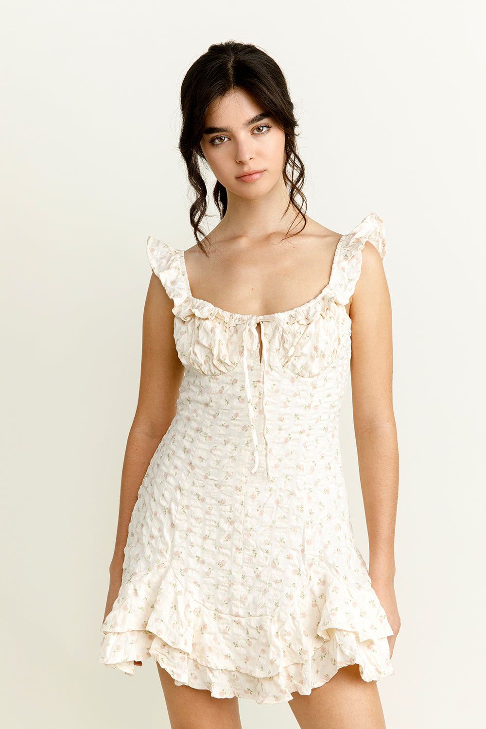 Woman wearing an ivory floral mini dress with ruffled straps against a plain background