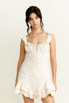Woman wearing an ivory floral mini dress with ruffled straps against a plain background
