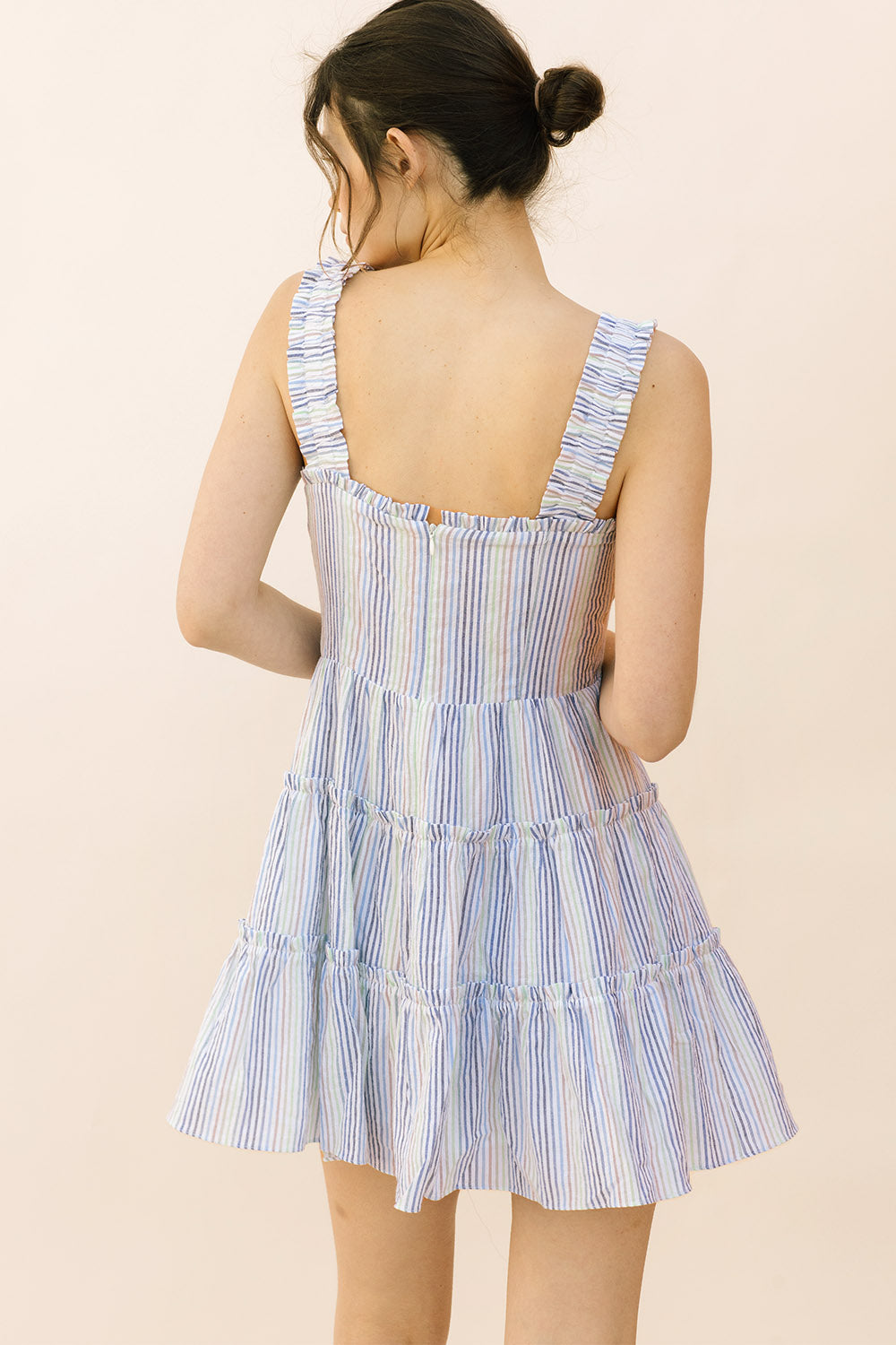 Back view of a woman wearing a blue and white striped dress on a beige background