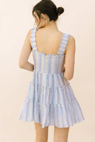 Back view of a woman wearing a blue and white striped dress on a beige background