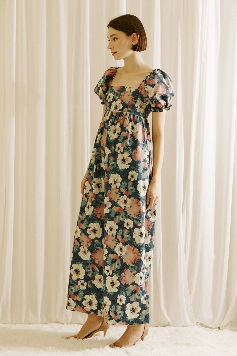 A woman modeling a flowy jumpsuit standing in front of white curtains