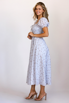 Side view of a model wearing a blue base midi dress with pink florals, a fully smocked bodice, puff sleeves, and a flowy midi skirt.