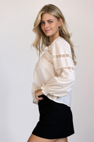Side view of a model wearing a long sleeve top with textured Swiss dot, lace paneling and puff sleeves.