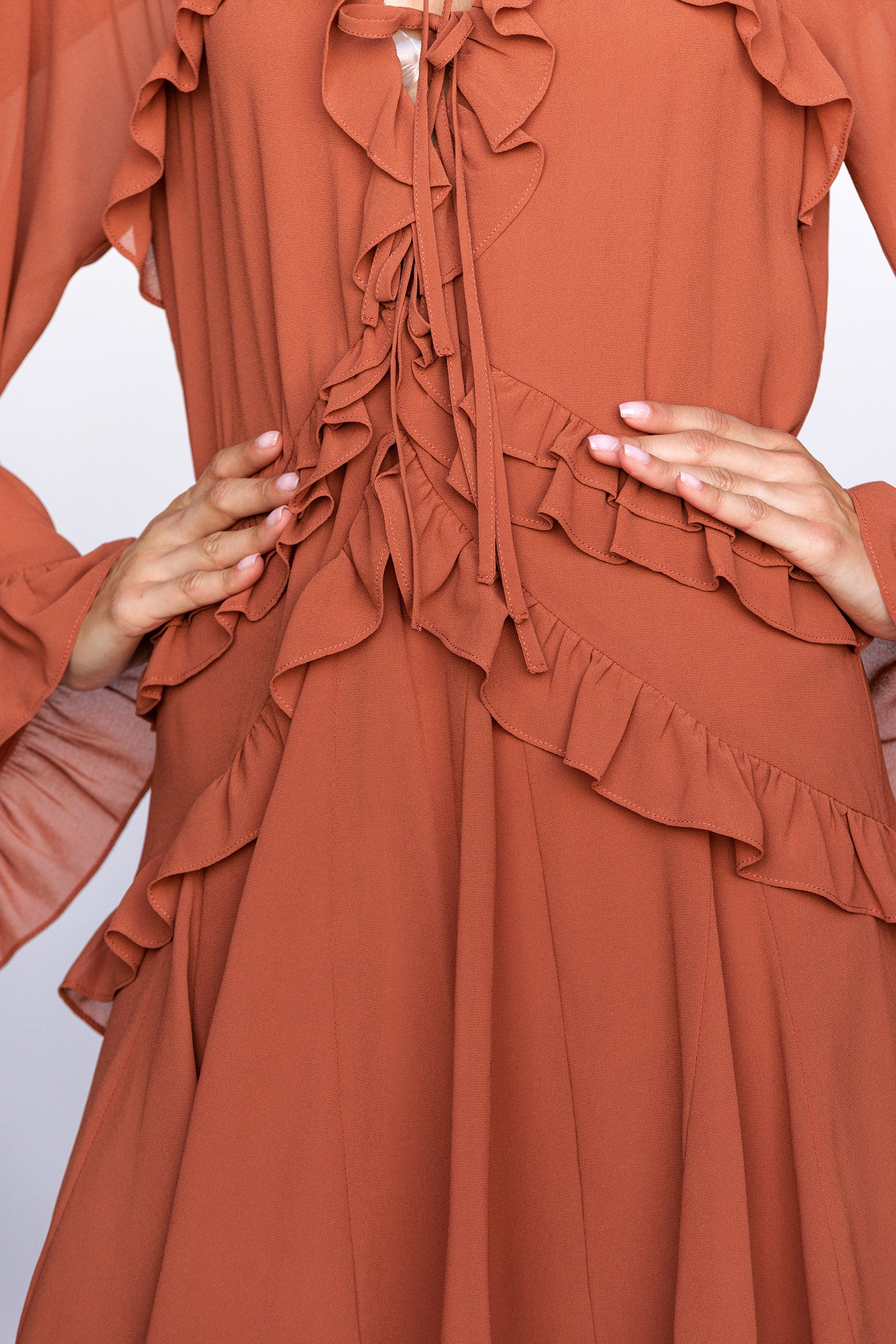 Rust-colored dress with ruffled details being modeled against a light background