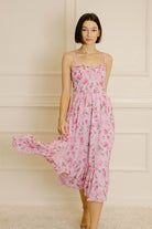 Woman wearing a pink floral dress against a neutral wall.
