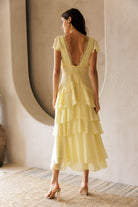 Back view of a model wearing a yellow dress standing in a room with a textured wall.