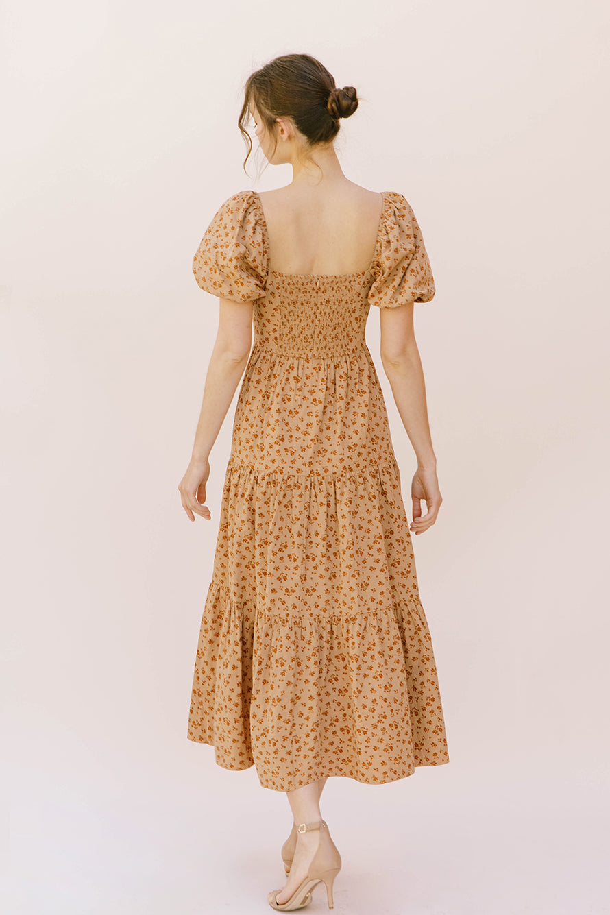 Back view of a woman wearing a brown floral midi dress on a plain background
