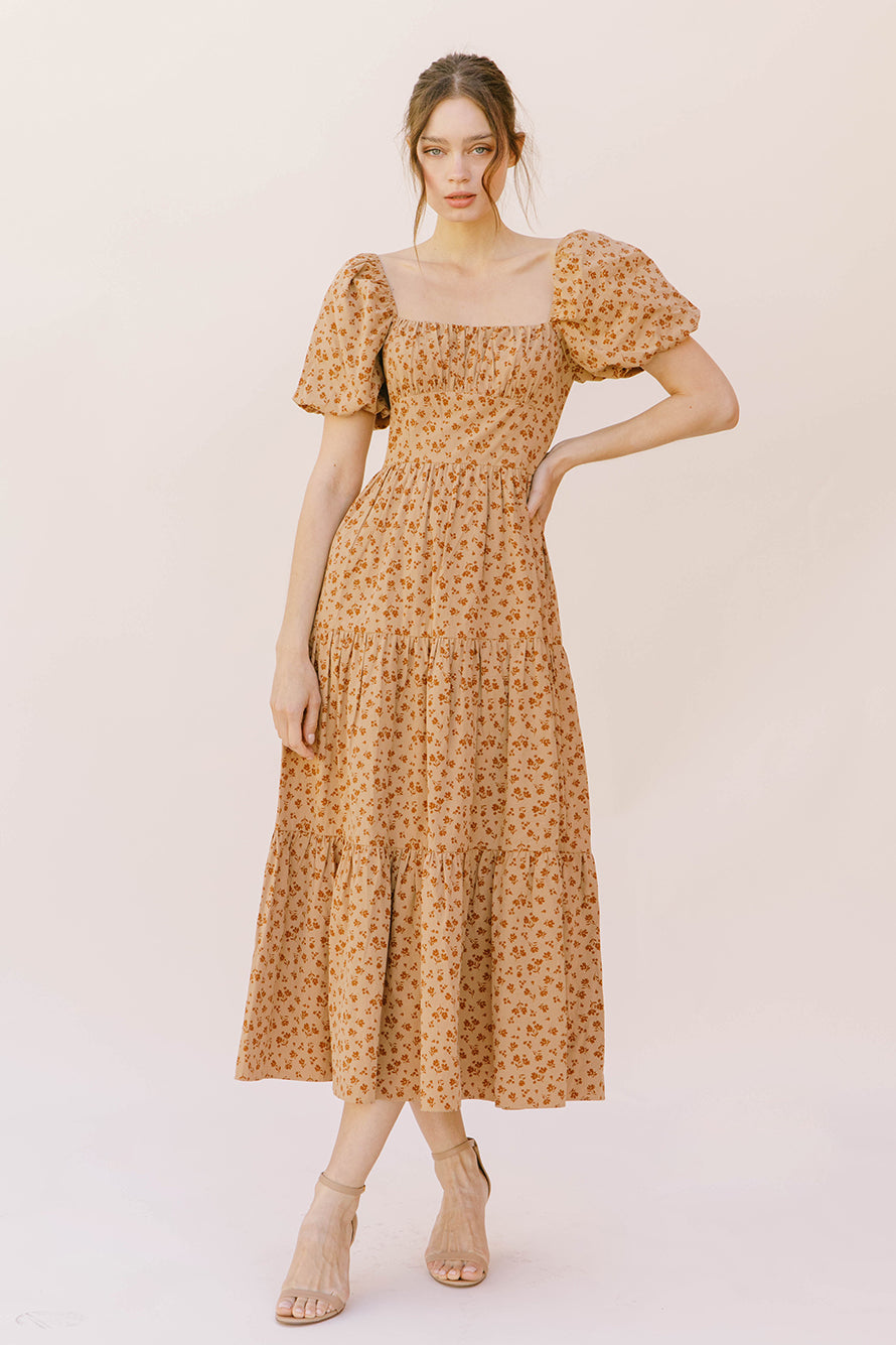Woman wearing a brown floral midi dress on a plain background