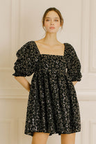 Woman wearing a black dress with star pattern against a neutral wall