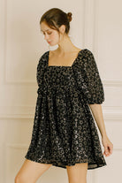 Woman wearing a black dress with sequin star pattern against a neutral background