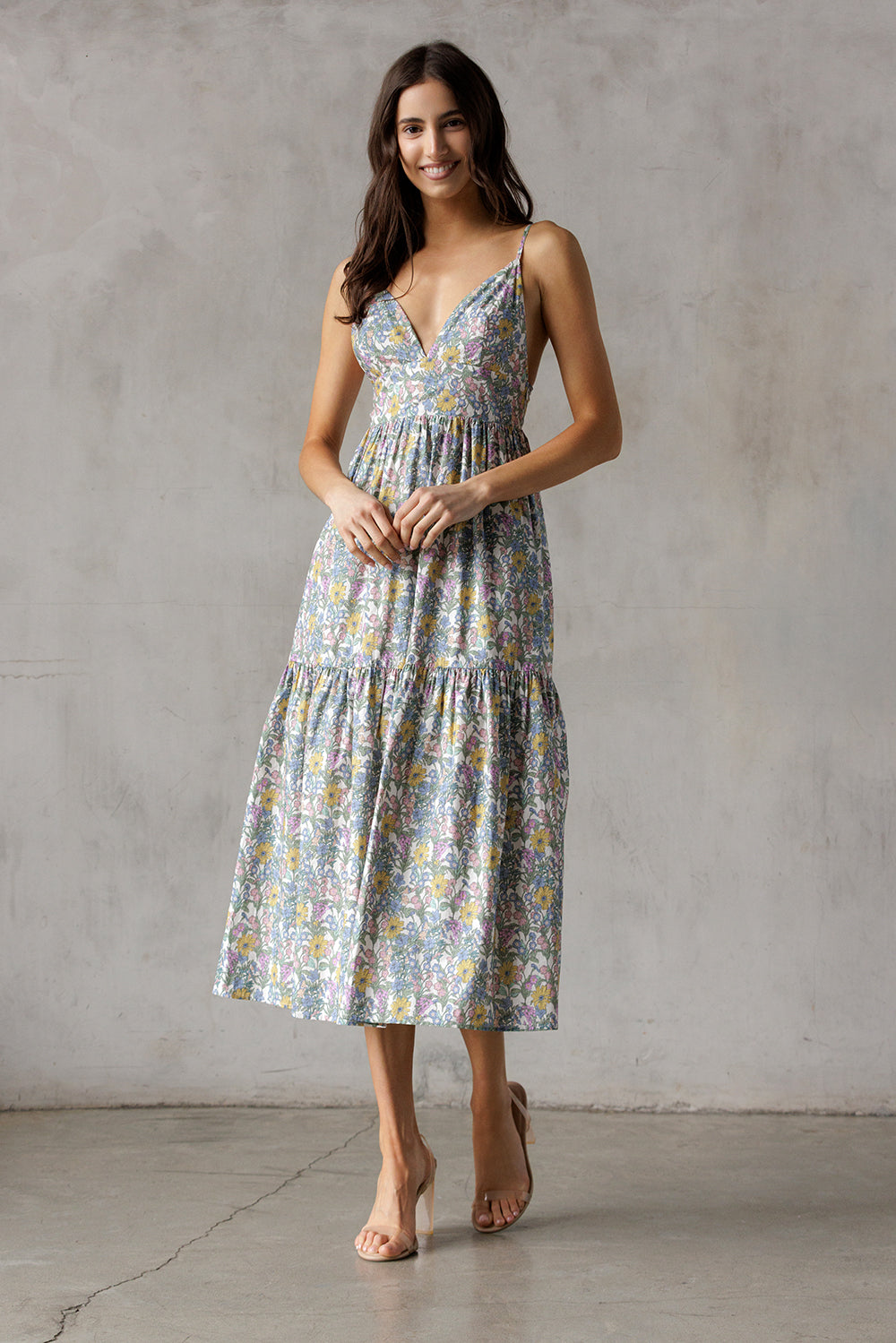 A woman wearing a floral midi dress with a fitted bodice, deep V-neckline, and adjustable spaghetti straps.