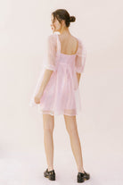 Back view of a woman wearing a pink sequin dress with sheer sleeves on a white background