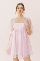 Woman wearing a pink sequin dress with sheer sleeves against a neutral pink background