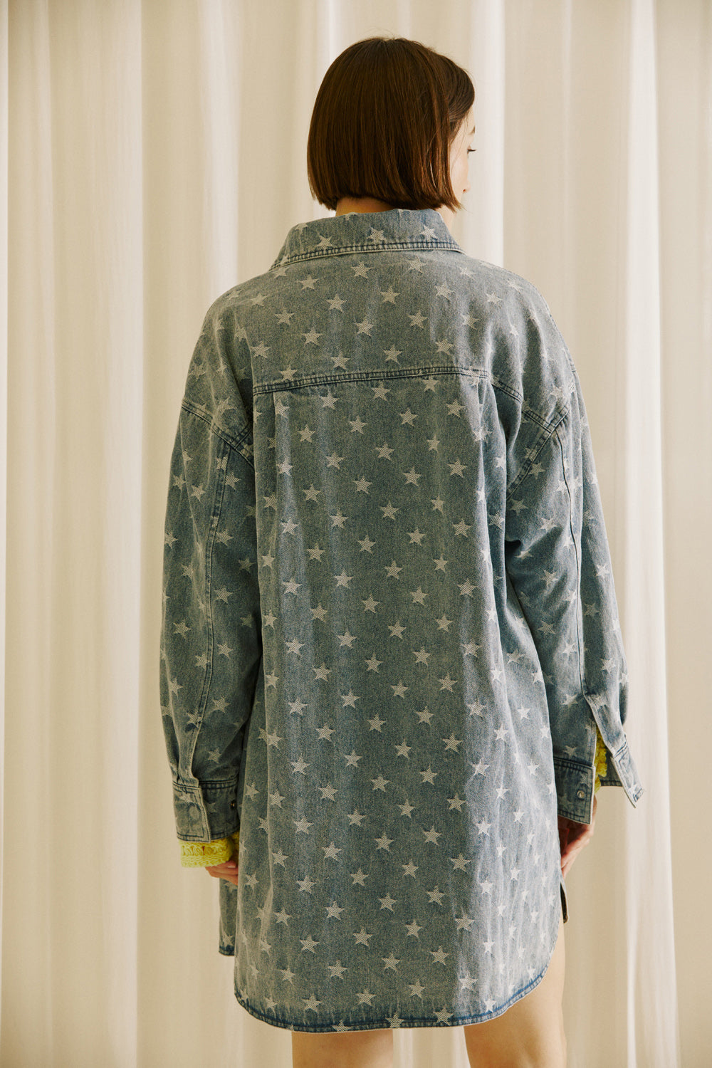 Back view of a woman wearing a star-patterned denim jacket against a neutral background
