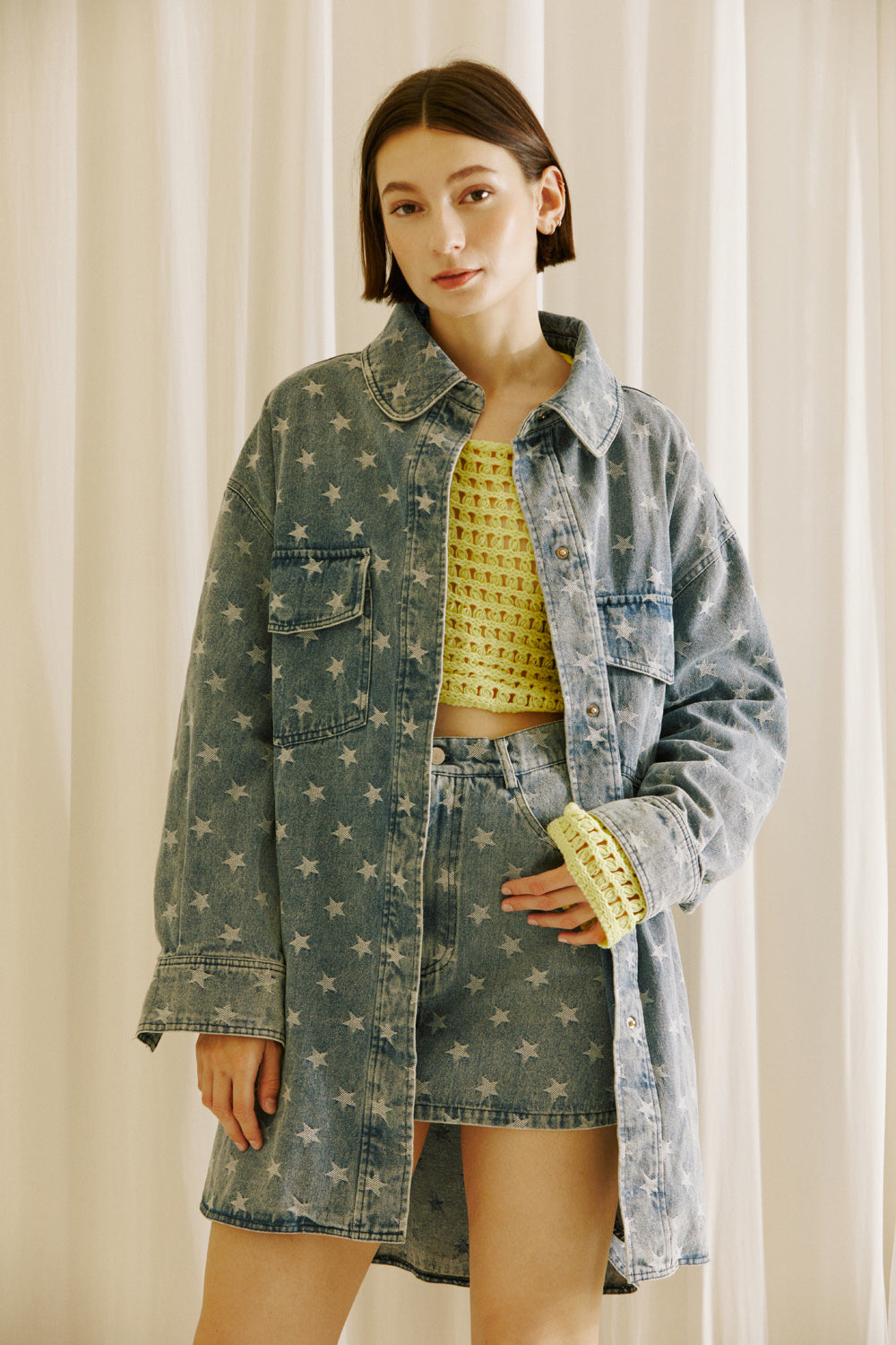 Woman wearing a star-patterned denim jacket and skirt with a yellow top against a neutral background