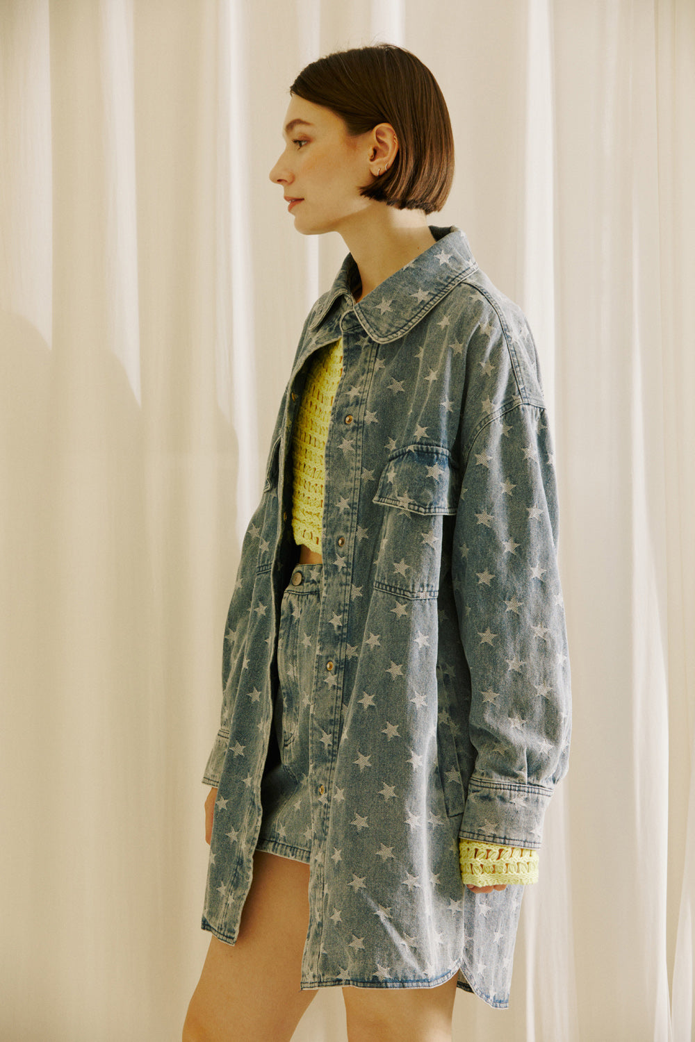 Side view of a woman wearing a star-patterned denim jacket and skirt with a yellow top against a neutral background