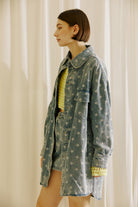 Side view of a woman wearing a star-patterned denim jacket and skirt with a yellow top against a neutral background