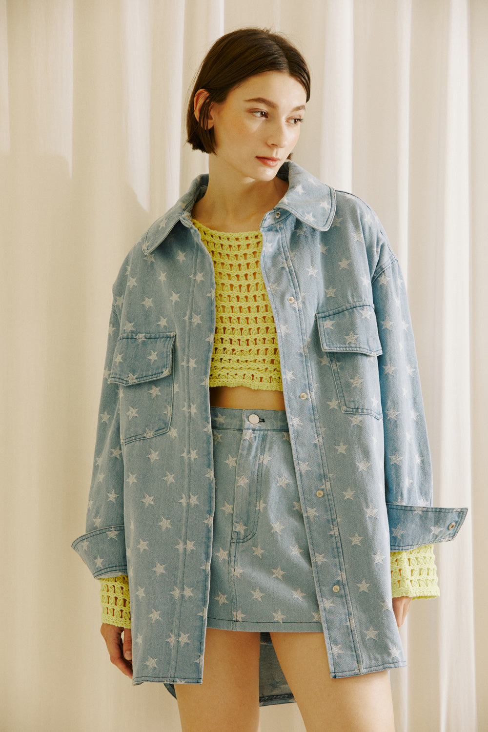 A model wearing a yellow crochet top and star-patterned denim jacket and skirt set against a neutral background