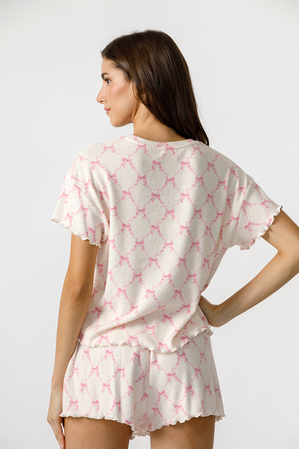 Woman wearing a pink and white pajama set with bow pattern on a plain background