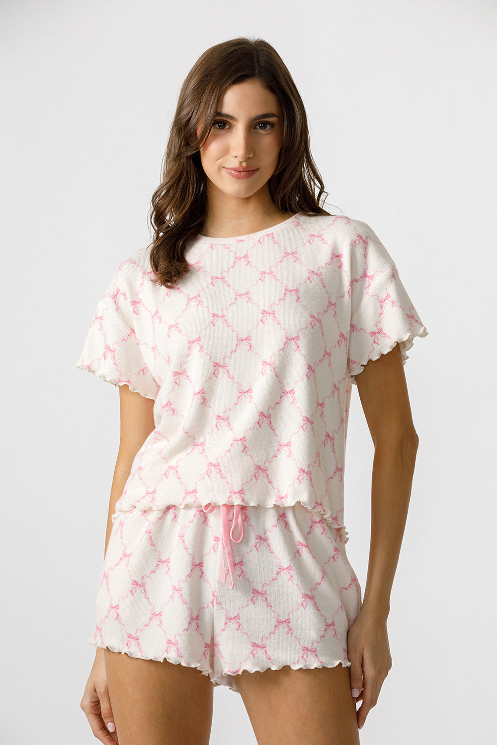 Front view of a woman wearing a pink and white pajama set with bow pattern on a plain background