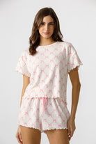 Front view of a woman wearing a pink and white pajama set with bow pattern on a plain background