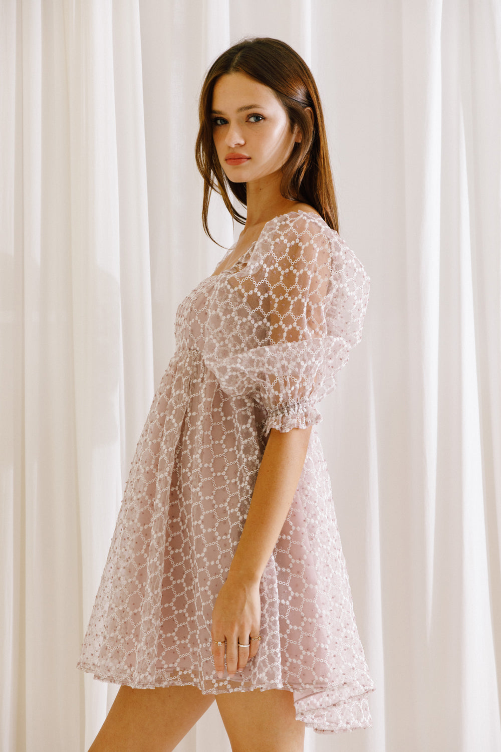 Side view of a model wearing a lilac mini dress with mini daisies embroidery and puffy sleeves