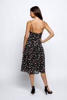 Back view of a woman wearing a black floral dress on a white background