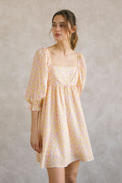 Woman wearing a pink and orange floral dress against a plain background