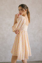 Side view of a woman wearing a pink and orange floral dress against a plain background