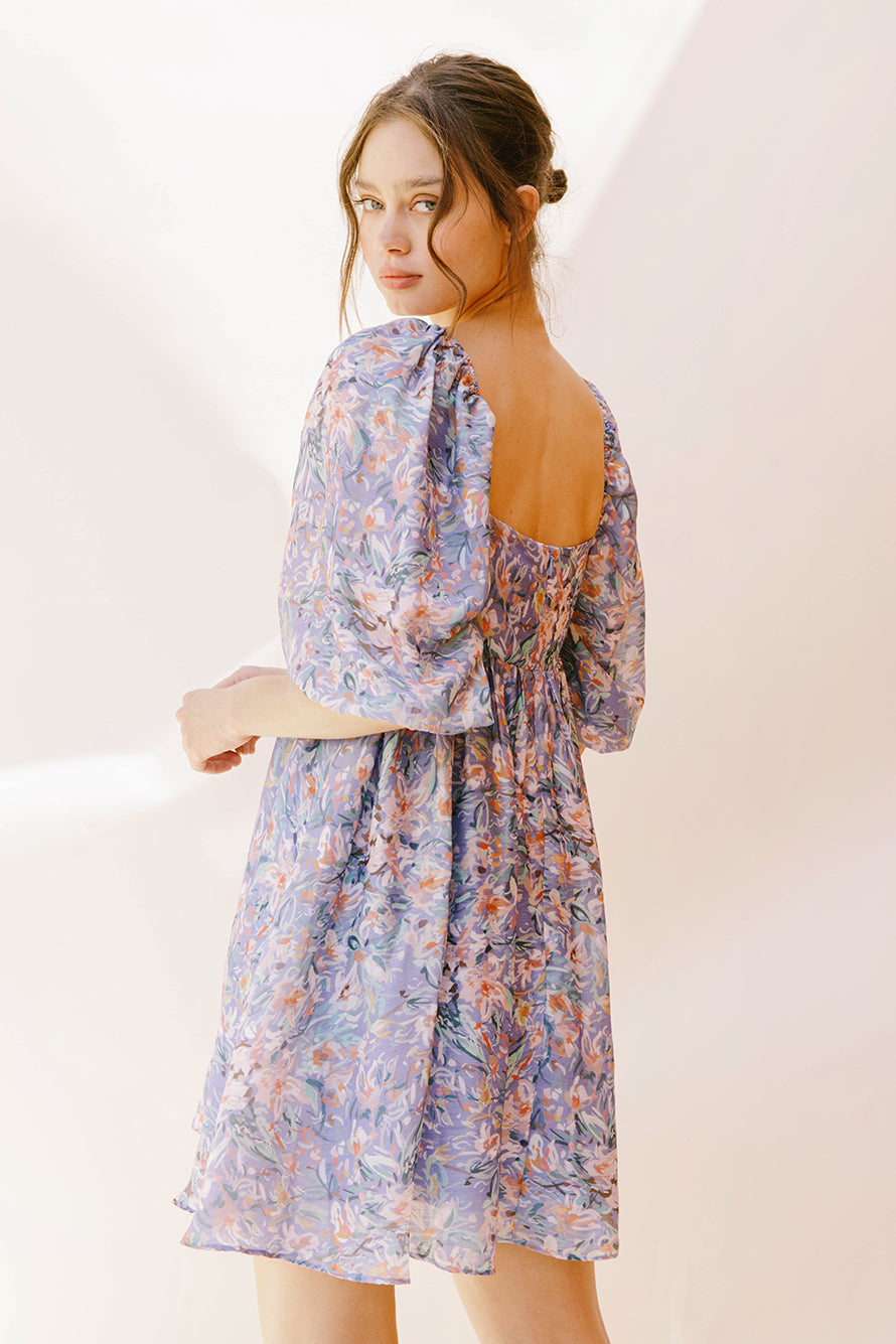 Back view of a woman wearing a purple paint stroke print dress against a plain background